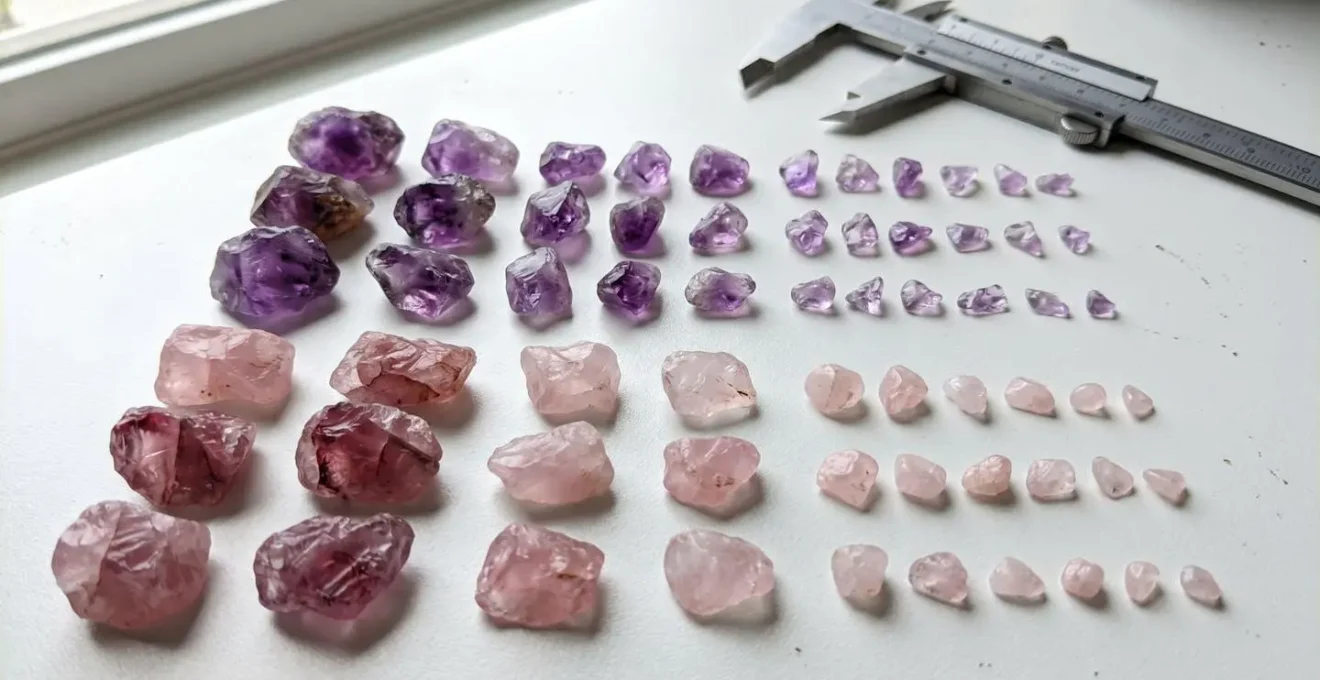 Gros plan sur des améthystes et des quartz roses triés par taille, alignés sur une surface blanche épurée avec un pied à coulisse visible en arrière-plan flouté